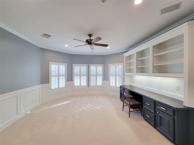 unfurnished office featuring crown molding, ceiling fan, built in desk, and light carpet