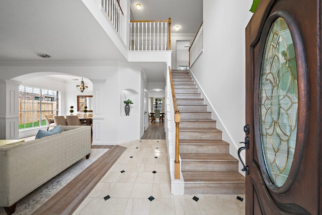 entryway with ornamental molding, arched walkways, a high ceiling, and light tile patterned floors