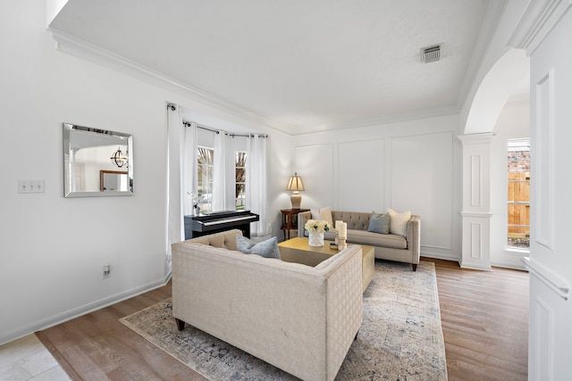 living area featuring arched walkways, a decorative wall, visible vents, decorative columns, and crown molding