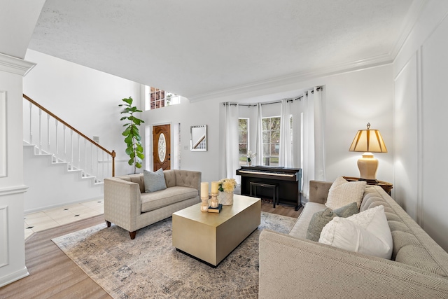 living room with stairway, light wood-type flooring, decorative columns, and crown molding