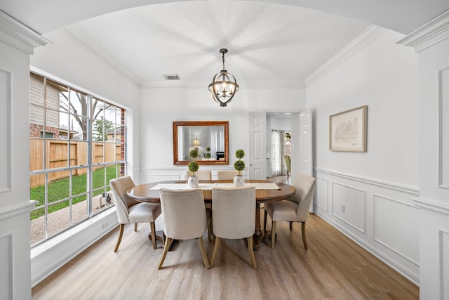 dining area with light wood-style flooring, a notable chandelier, visible vents, ornamental molding, and wainscoting