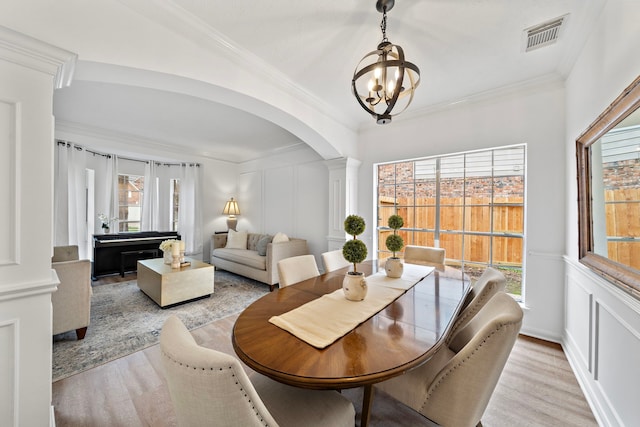 dining space featuring a decorative wall, visible vents, light wood-type flooring, decorative columns, and crown molding