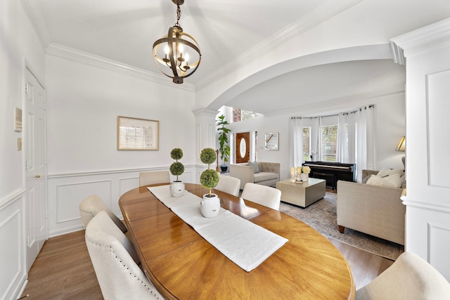 dining space with arched walkways, wood finished floors, crown molding, ornate columns, and a notable chandelier