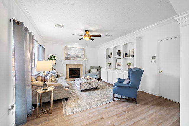 living room with ornamental molding, light wood-type flooring, a fireplace, and visible vents