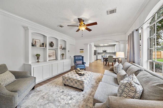 living room featuring decorative columns, visible vents, arched walkways, and wood finished floors