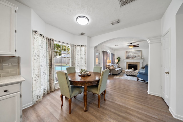 dining room with arched walkways, visible vents, a tiled fireplace, and light wood-style flooring