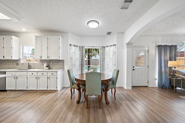 dining area with arched walkways, light wood-type flooring, visible vents, and plenty of natural light