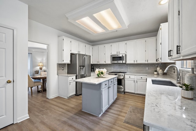 kitchen with a center island, stainless steel appliances, white cabinets, a sink, and light stone countertops