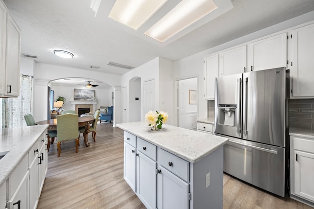 kitchen featuring arched walkways, a fireplace, white cabinetry, a kitchen island, and stainless steel fridge with ice dispenser