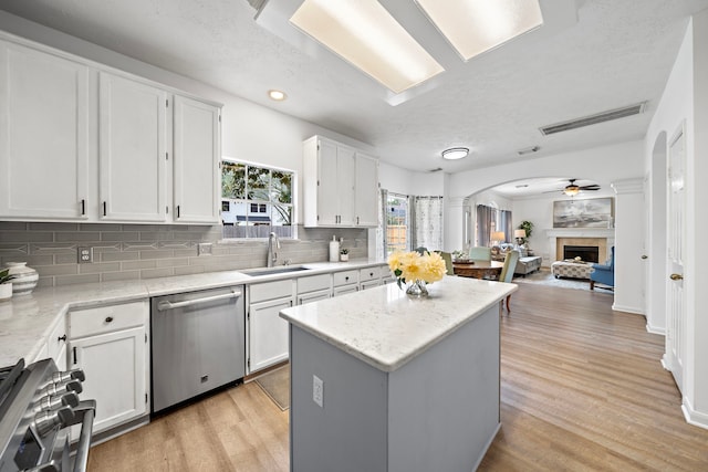 kitchen featuring stove, open floor plan, stainless steel dishwasher, white cabinetry, and a sink