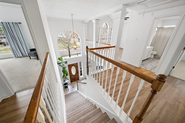 staircase featuring a textured ceiling, wood finished floors, attic access, and ornate columns