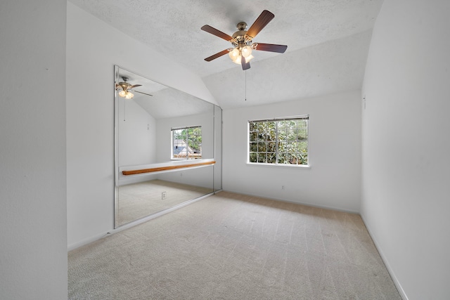 unfurnished room featuring light carpet, a textured ceiling, vaulted ceiling, and baseboards