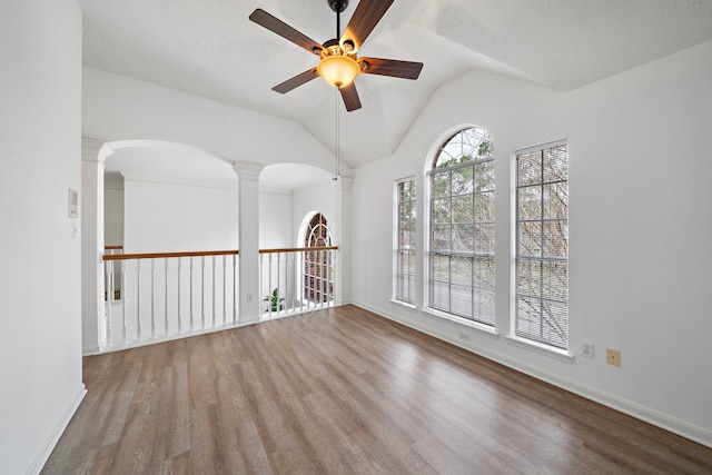 empty room featuring decorative columns, ceiling fan, vaulted ceiling, wood finished floors, and baseboards