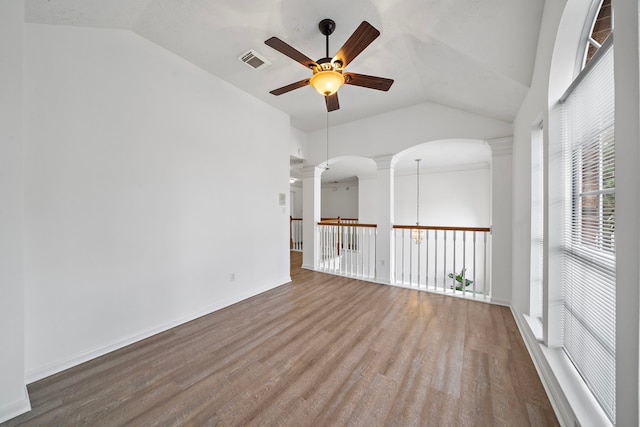 empty room with vaulted ceiling, visible vents, decorative columns, and wood finished floors