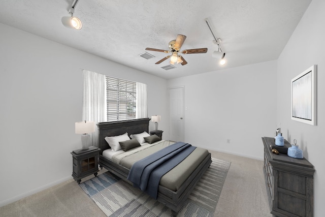 bedroom with rail lighting, visible vents, a textured ceiling, and light colored carpet