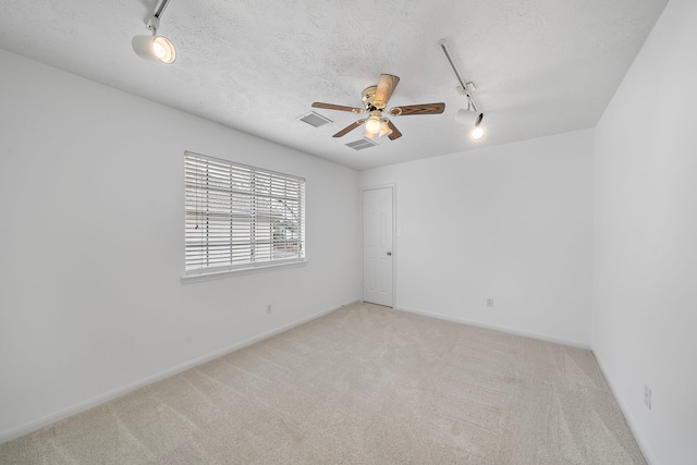 empty room with light carpet, track lighting, visible vents, and a textured ceiling