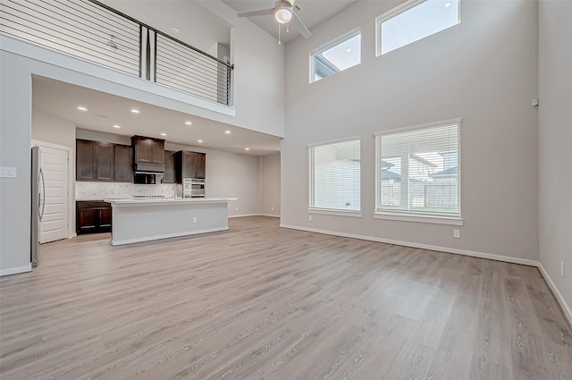 unfurnished living room featuring light hardwood / wood-style flooring, ceiling fan, and a high ceiling