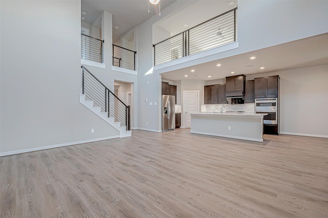 unfurnished living room with a towering ceiling, sink, and light wood-type flooring