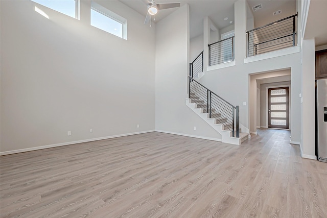 unfurnished living room featuring ceiling fan, light wood-type flooring, a high ceiling, and a wealth of natural light