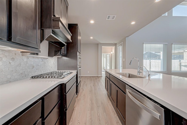 kitchen featuring sink, backsplash, light hardwood / wood-style floors, dark brown cabinetry, and stainless steel appliances