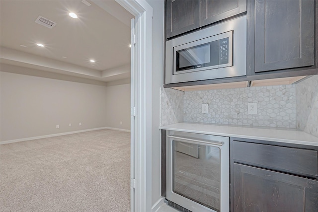 kitchen with light carpet, stainless steel microwave, beverage cooler, and decorative backsplash