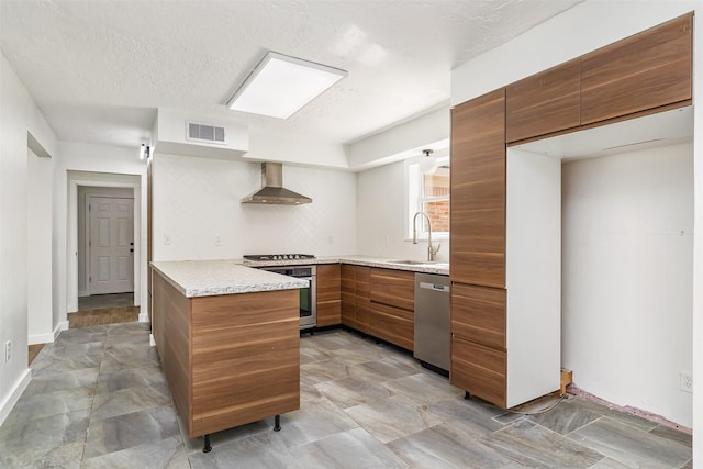 kitchen featuring wall chimney range hood, sink, appliances with stainless steel finishes, tasteful backsplash, and kitchen peninsula