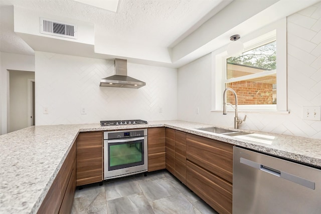 kitchen with stainless steel appliances, sink, wall chimney range hood, and light stone counters