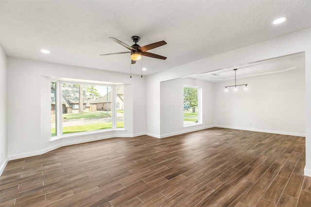 unfurnished room featuring plenty of natural light, dark hardwood / wood-style floors, ceiling fan with notable chandelier, and a textured ceiling