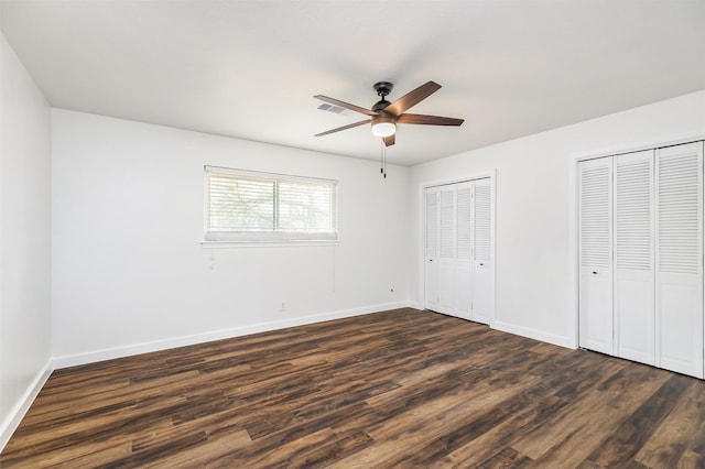 unfurnished bedroom with multiple closets, ceiling fan, and dark hardwood / wood-style flooring