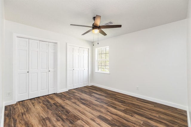 unfurnished bedroom with multiple closets, ceiling fan, and dark wood-type flooring