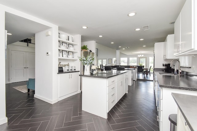 kitchen with dark parquet floors, white cabinetry, sink, a center island, and black electric cooktop