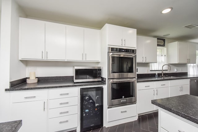 kitchen with sink, dark wood-type flooring, appliances with stainless steel finishes, white cabinetry, and wine cooler