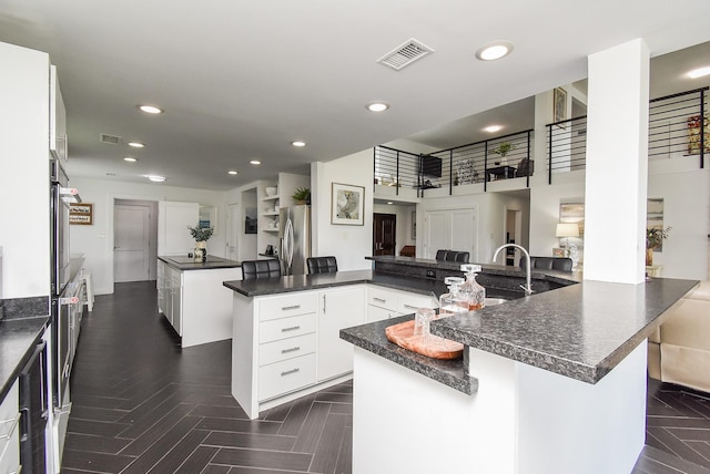 kitchen with a large island with sink, white cabinetry, appliances with stainless steel finishes, and kitchen peninsula