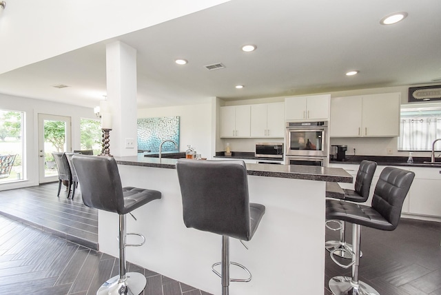 kitchen featuring white cabinetry, sink, a breakfast bar, and stainless steel double oven