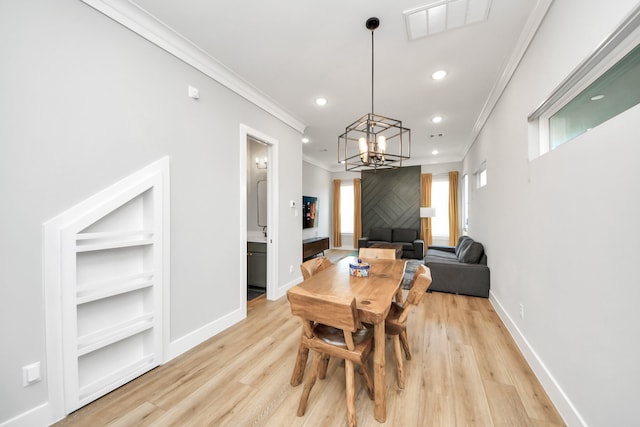 dining area featuring built in shelves, crown molding, a chandelier, and light hardwood / wood-style flooring