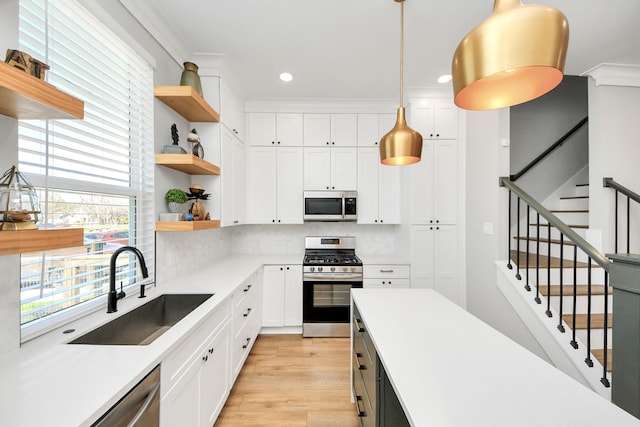 kitchen with white cabinetry, stainless steel appliances, decorative light fixtures, and sink