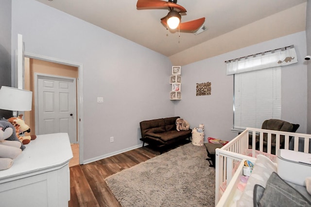 bedroom with a crib, vaulted ceiling, dark wood-type flooring, and ceiling fan