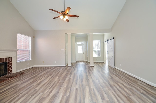 unfurnished living room featuring plenty of natural light, ceiling fan, a barn door, and a brick fireplace