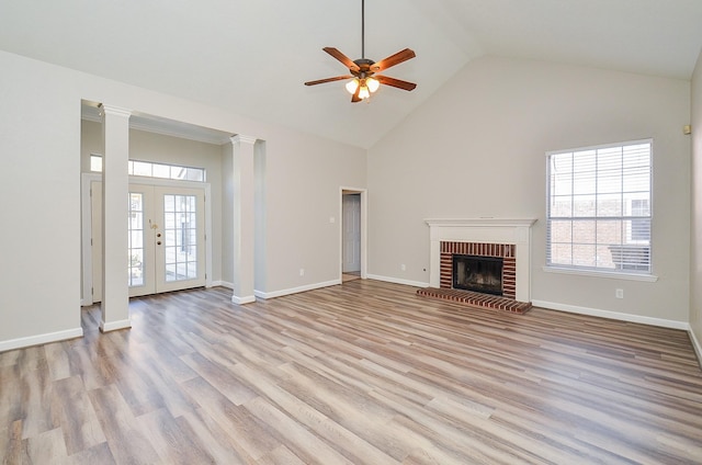 unfurnished living room featuring a healthy amount of sunlight, a brick fireplace, decorative columns, and light wood finished floors