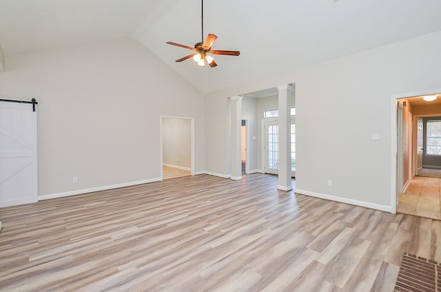 unfurnished living room featuring a barn door, light wood-style floors, ceiling fan, ornate columns, and high vaulted ceiling