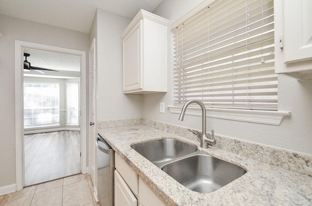 kitchen featuring light stone counters, light tile patterned flooring, a sink, white cabinets, and stainless steel dishwasher