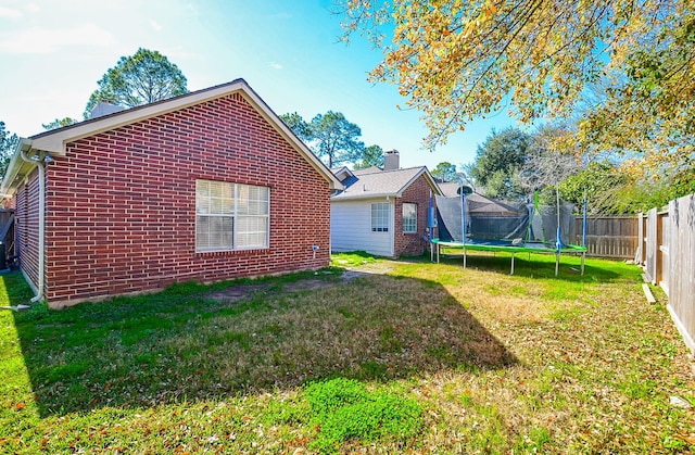 exterior space with brick siding, a trampoline, a fenced backyard, and a lawn