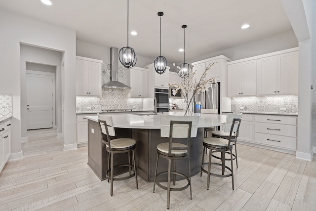 kitchen with white cabinets, hanging light fixtures, a center island with sink, and wall chimney range hood