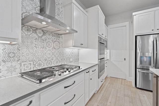 kitchen with white cabinetry, backsplash, stainless steel appliances, light wood-type flooring, and wall chimney exhaust hood