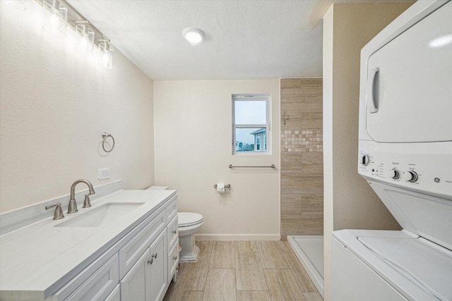 bathroom with vanity, stacked washer / drying machine, tiled shower, toilet, and a textured ceiling