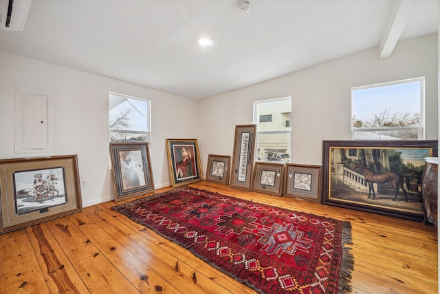 living area featuring beamed ceiling, hardwood / wood-style floors, and electric panel