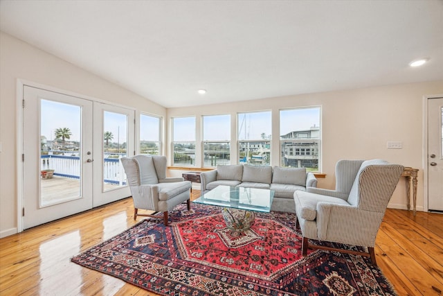 living room featuring lofted ceiling, french doors, a water view, and light wood-type flooring