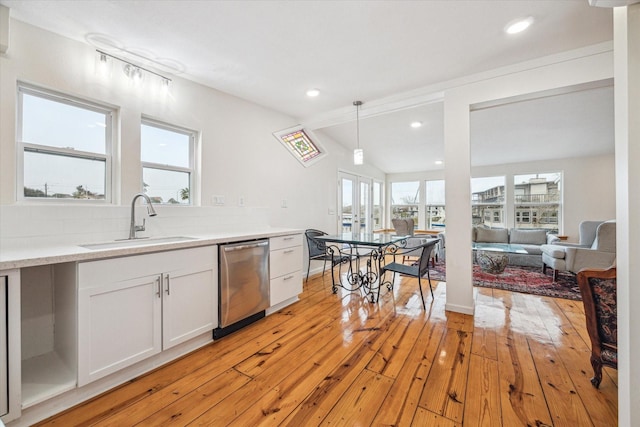 kitchen with sink, white cabinets, decorative light fixtures, stainless steel dishwasher, and light wood-type flooring