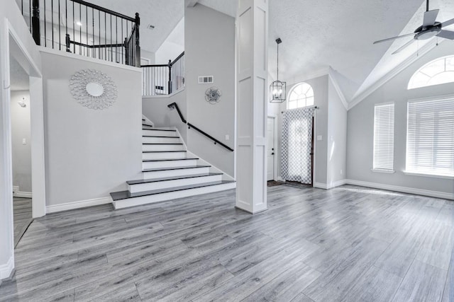 foyer entrance featuring visible vents, stairway, wood finished floors, high vaulted ceiling, and ceiling fan with notable chandelier