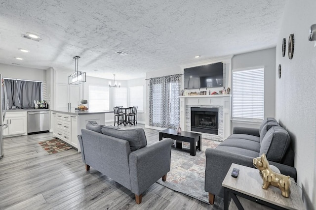 living area featuring a textured ceiling, light wood-type flooring, a fireplace, and visible vents